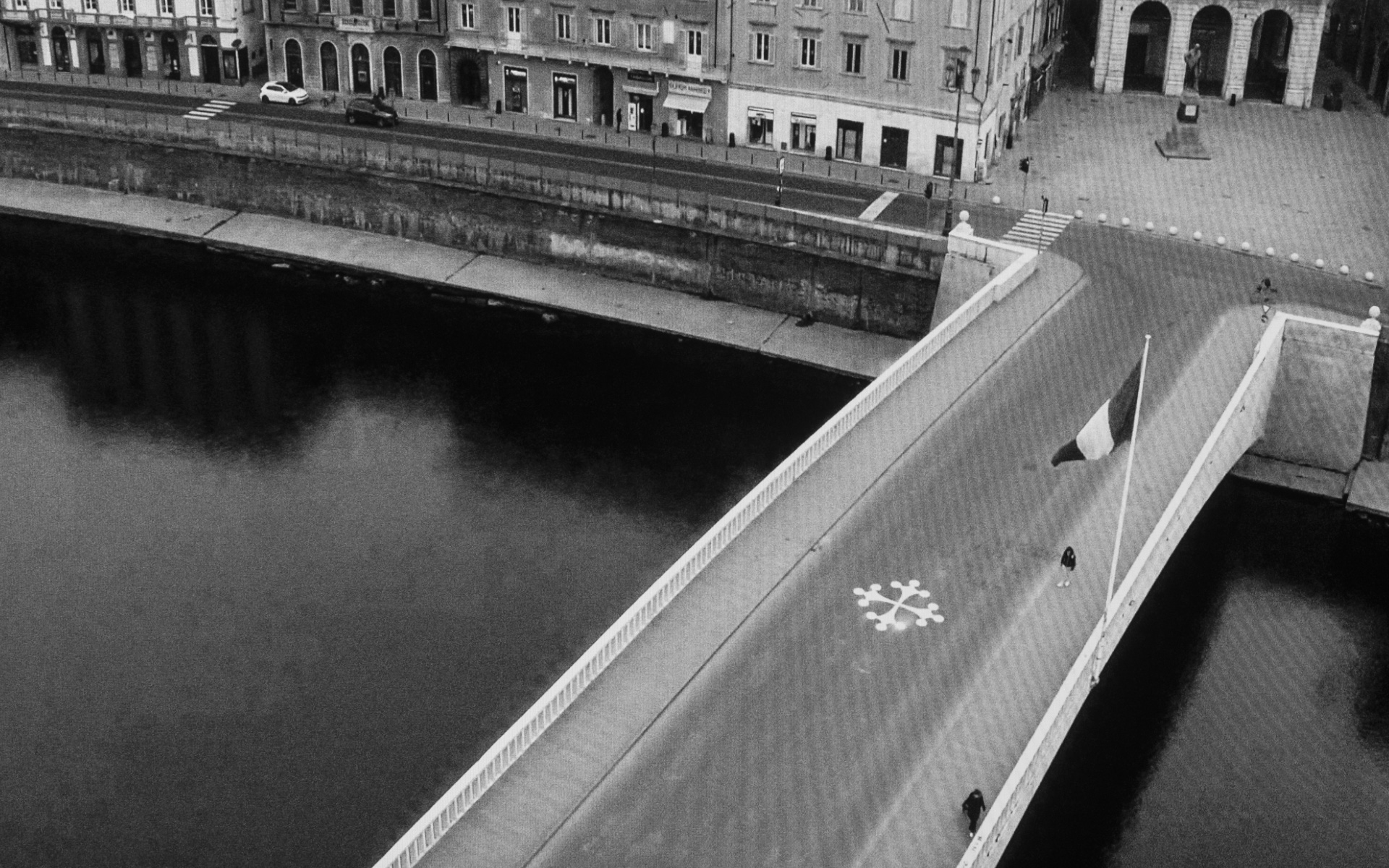 Pisa, Mezzo Bridge and Garibaldi Square - Two lonely figures crossing the bridge over the river Arno near the famous leaning tower of Pisa, March 26. 2020.